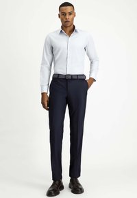 Camicia azzurro chiaro con maniche lunghe abbinata a pantaloni navy e una cintura a fantasia. Scarpe eleganti nere completano l'outfit.