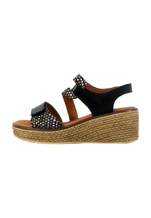 Sandale à talon noir avec des accents cloutés, semelle style espadrille tissée et brides ouvertes. Cuir lisse et détails texturés sur les brides.