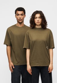 Πράσινα βαμβακερά T-shirts με κοντά μανίκια, με στρογγυλή λαιμόκοψη και μικρή κεντημένη λεπτομέρεια μπροστά, σε συνδυασμό με σκουρόχρωμα τζιν.