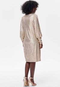 Złota sukienka z cekinami, z długimi bufkami na rękawach, do kolan, o prostym kroju, gładkiej fakturze. W połączeniu z cielistymi szpilkami z widocznym paskiem wokół kostki.