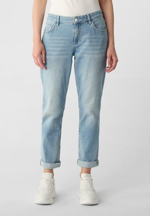 Light blue cuffed jeans worn by person with white sneakers, shown from waist to feet against plain background.