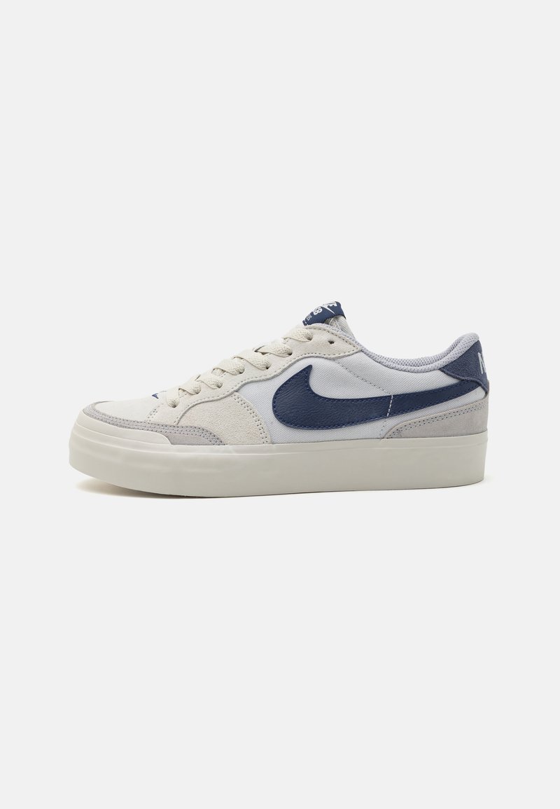 Nike-sko med overdeler i semsket lær og tekstil i lys grå og marineblå, med en hvit gummisåle og logoakkenter.