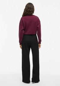 Pullover bourgogne à coupe décontractée et encolure ronde, associé à un pantalon noir texturé à jambes larges avec taille élastique.