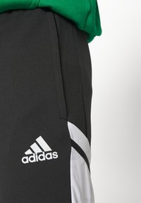 Schwarze Sporthosen mit weißen Seitenpaneelen und einem Adidas-Logo. Hergestellt aus einem glatten, dehnbaren Stoff. Enganliegende Passform mit Taschen.