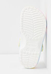 Hvide Crocs såler med tekstureret mønster, der har et gradientdesign, der går fra gul til pink og blå kanter.
