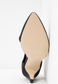 Chaussure à talon haut noire à bout pointu vue de la semelle beige lisse avec un talon aiguille fin.