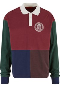 Langærmet polo-shirt med et farveblock design i bordaux og grøn, hvid krave, treknapper foran og et emblem på brystet.