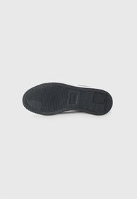 Black rubber shoe sole with textured surface, featuring a PUMA logo and a pronounced tread pattern for grip.