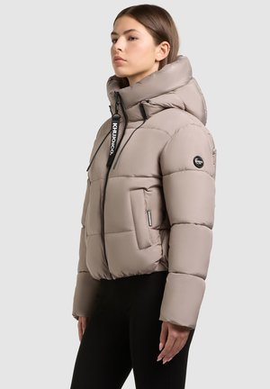 Lightweight beige puffer jacket with a high collar, front zipper, and black logo accents. Features side pockets and soft, quilted texture.