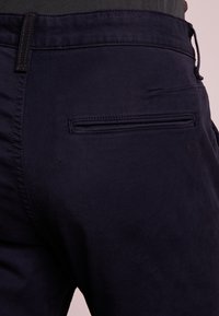 Pantaloni navy in cotone con una texture liscia, dotati di una tasca posteriore con chiusura a zip e un logo discreto.