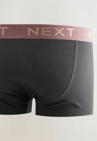 Svarta boxertrosor med en ribbad vinröd midjeresår som har präglad text "NEXT". Slät tyg med en åtsittande passform och platta sömmar.