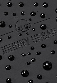 Fekete texturált felület, rajta kiemelkedő "JOHNNY URBAN" logóval. A felületen különböző méretű, fényes fekete cseppek szórva találhatók.