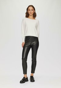 Pull en maille blanche avec ourlet côtelé, associé à un pantalon skinny en simili cuir noir. Le modèle porte des mocassins noirs. Design simple et moderne.