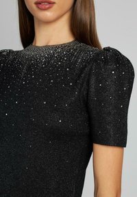 Czarna błyszcząca sukienka z krótkimi bufkami, ozdobiona srebrnymi ćwiekami i teksturowanym dekoltem, tworząca gradientowy wzór.