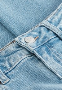 Jeans de mezclilla de color azul claro con un botón de metal plateado, costuras en tono beige y una textura suave con un ligero efecto de decoloración.