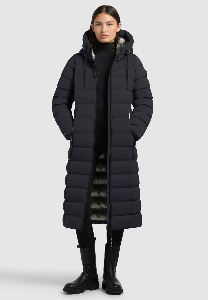 Cappotto lungo imbottito di un nero intenso, dotato di cappuccio, chiusura con zip e tasche laterali; esterno trapuntato e fodera interna a contrasto.