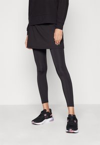 Robe de sport noire superposée sur des leggings noirs, associée à des baskets noires avec des accents roses et une semelle extérieure à motifs. Textures lisses tout au long.