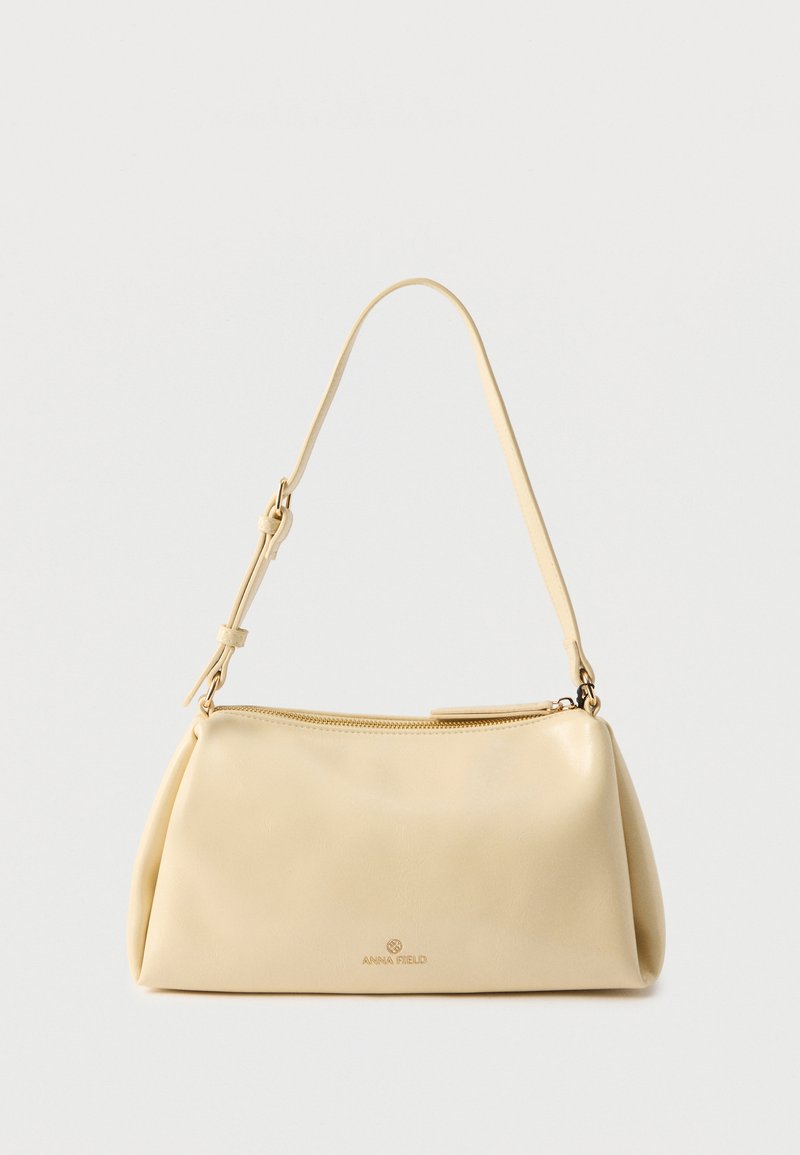 Sac bandoulière rectangulaire beige avec sangle réglable et fermeture éclair, comportant un petit logo "Anna Field" au centre avant.