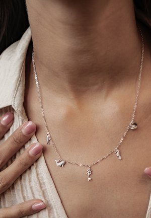 Delicate silver chain necklace with ocean-themed charms, including a shell, fish, mermaid, seahorse, and starfish, worn on bare skin.