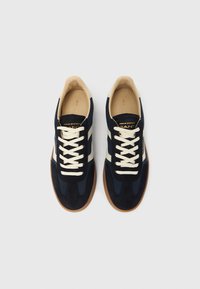 Par modro-belih superg GANT z kremastimi vezalkami in gumijastimi podplati, pogled iz zgornje strani na belem ozadju.