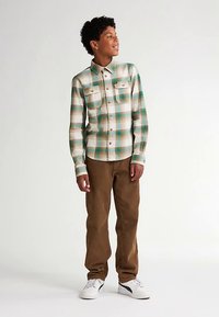 Košile na knoflíky s károvaným vzorem v krémové, tyrkysové a hnědé barvě se dvěma náprsními kapsami. Kombinovaná s hnědými kalhotami a bílými teniskami, představující pohodlný střih.