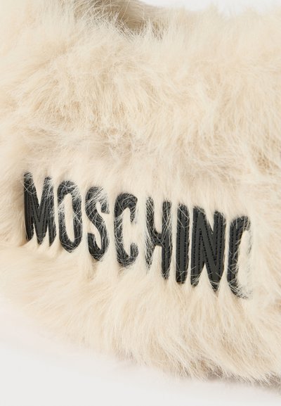 Dirbtinio kailio medžiaga kremine spalva su tekstūruotais plaukais; jame užfiksuotas „MOSCHINO“ logotipas ryškiomis juodomis raidėmis.