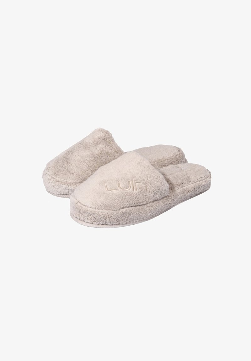 Beige, fluffy slippers with a soft texture, open back, and rounded toe design. Features embroidered logo on the front.