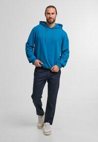 Blue hoodie with a drawstring hood, long sleeves, and ribbed cuffs. Paired with navy pants and white sneakers. Simple, casual look.