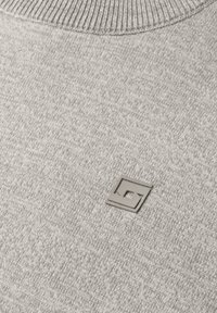 Tissu tricoté gris clair avec un petit logo carré en relief présentant un motif géométrique près du col.