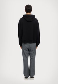 Schwarzer Kapuzenpullover mit lockerer Passform, kombiniert mit grauen geraden Jeans. Der Stoff wirkt weich und hat minimale Details.