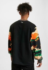 Black sweatshirt featuring colorful pixelated camouflage sleeves in orange, green, and beige; ribbed collar and cuffs; casual fit.