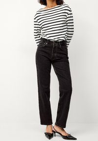 Jeans neri a vita alta e una maglietta a righe bianche e nere a maniche lunghe. La maglietta ha un collo ampio; i jeans presentano tasche frontali.