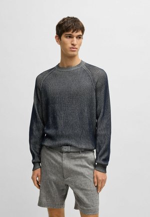Pull en tricot rayé bleu marine avec un col rond et des manches longues, associé à un short gris clair avec passants de ceinture et poches avant.