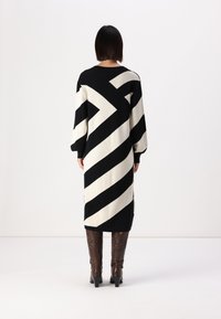 Robe pull à rayures noires et blanches avec des manches longues, une coupe décontractée, des fentes sur les côtés et des bottes marron jusqu'au genou.