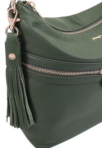 Groene leren handtas met gouden hardware, voorzien van een ritszak en een franjesleutelhangertje. Gladde textuur met een gestructureerde vorm.
