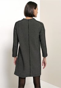 Musta-valkoinen kuvioitu mekko, jossa on kolme neljänneshihaa, pyöreä kaula-aukko ja suora leikkaus, takana keskellä sauma.