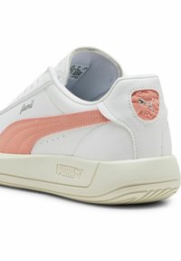 Béžové tenisky s ružovými akcentmi a logom Puma. Hladký kožený zvršok, vystužený golier a štruktúrovaná gumová podrážka. Nízky profil.