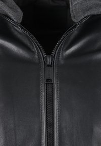 Zwarte leren jas met een ritssluiting aan de voorkant, met een grijze hoodie eraan bevestigd. Gladde textuur en een strak ontwerp. Ritspraken gemarkeerd met de merknaam.