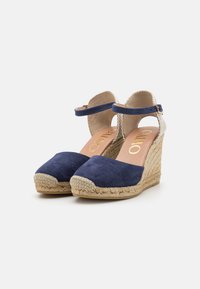 Bottines en suède bleu avec un talon en jute tressé, une sangle cheville et un dos beige clair. Marquage doré sur la semelle intérieure.