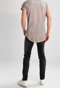 Šedé tričko s krátkým rukávem a zaobleným lemem, nošené s černými slim-fit džíny a bílými teniskami. Hladká textura, ležérní design.