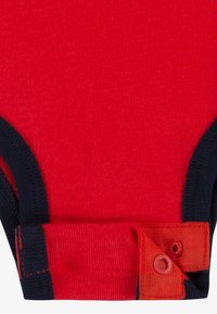 Rød bodysuit med marineblå trim, med trykknappet lukking nederst. Glatt, elastisk stoff med kontrasterende sømdetaljer.