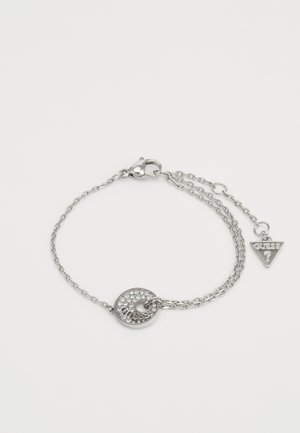 Bracciale in argento con un pendente circolare decorato con pietre trasparenti e un ciondolo triangolare inciso con la scritta "GUESS?"