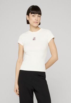 Hvit tettsittende T-skjorte med korte ermer, med en burgunder brodert "Salt & Olives"-logo på brystet. Kombinert med svarte bukser.