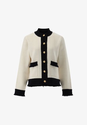Giacca intrecciata crema e nera con finitura testurizzata, caratterizzata da un colletto rotondo, chiusure anteriori con bottoni dorati e due tasche a contrasto.