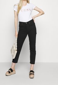 Hvid t-shirt med "GUESS" logo i rosaguld, parret med sorte højtaljede jeans og sorte platform sandaler med korksåler.