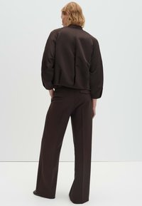 Bruine satijnen jas met een cropped model en gestructureerde schouders, gecombineerd met bijpassende bruine wijde broekspijpen. Gladde textuur, minimalistisch ontwerp.