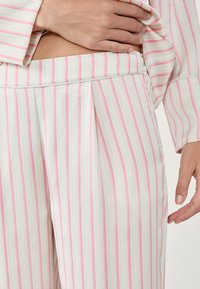 Tejido blanco con rayas verticales en rosa y gris claro; presenta un diseño plisado en la cintura y una textura suave. Manos visibles en los bordes.