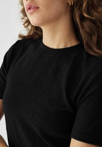 Fekete, rövidujjú póló puha anyagból, kerek nyakkivágással és sima textúrával. Közeli kép a gallér és a váll területéről.