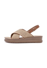 Wedge sandals featuring a cross-over woven strap design in light brown, with a tan adjustable ankle strap and textured rubber sole.