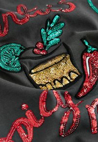 Black fabric featuring colorful sequin embroidery. Design includes green leaves, red chili peppers, and gold accents in a decorative format.